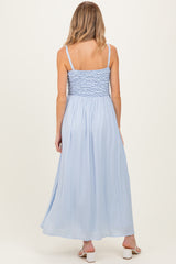 woman wearing a light blue maternity maxi dress with a smocked bodice and thin straps, showing her baby bump from the back