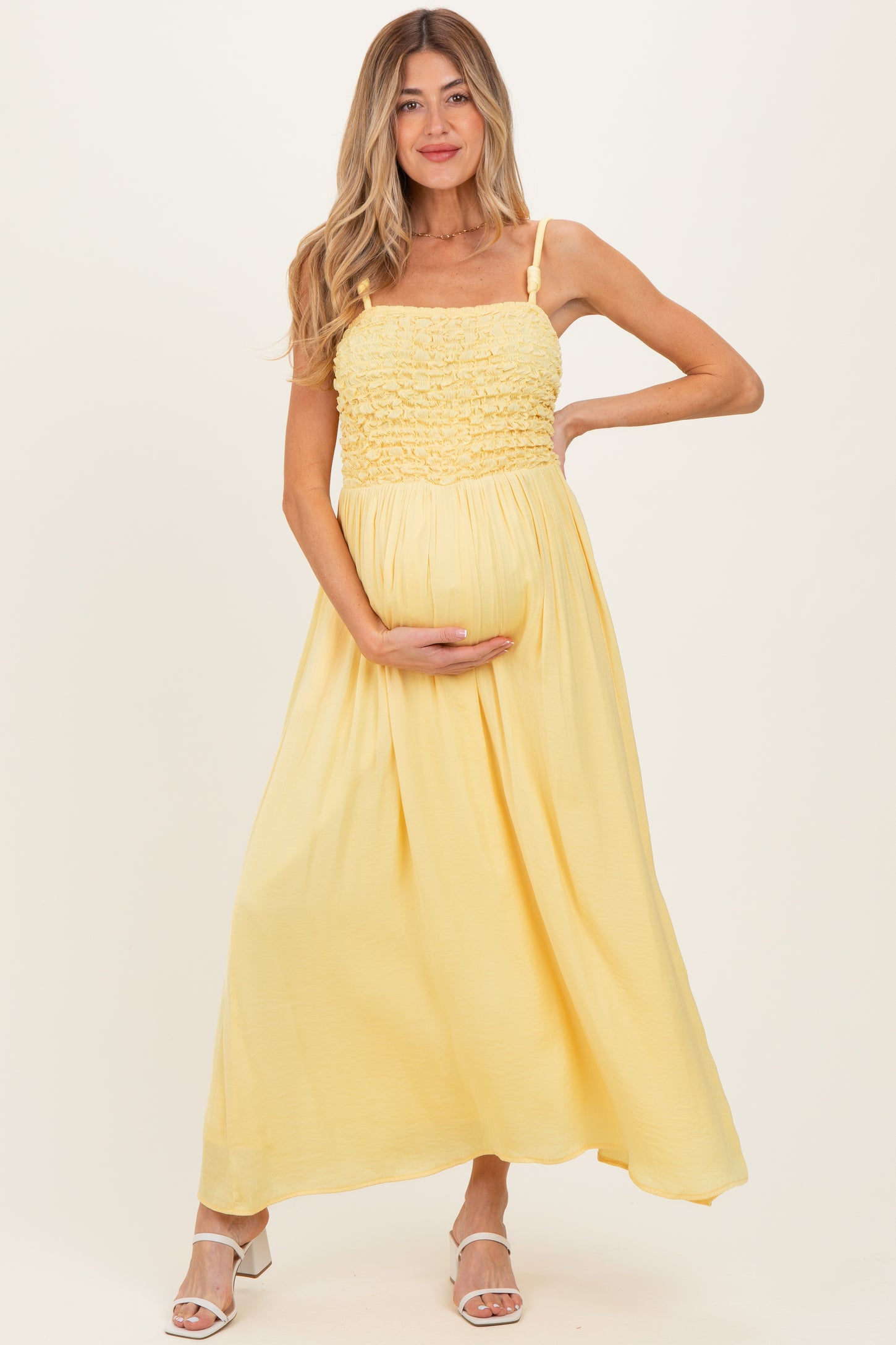 woman wearing a yellow maternity maxi dress with smocked bodice, holding her baby bump