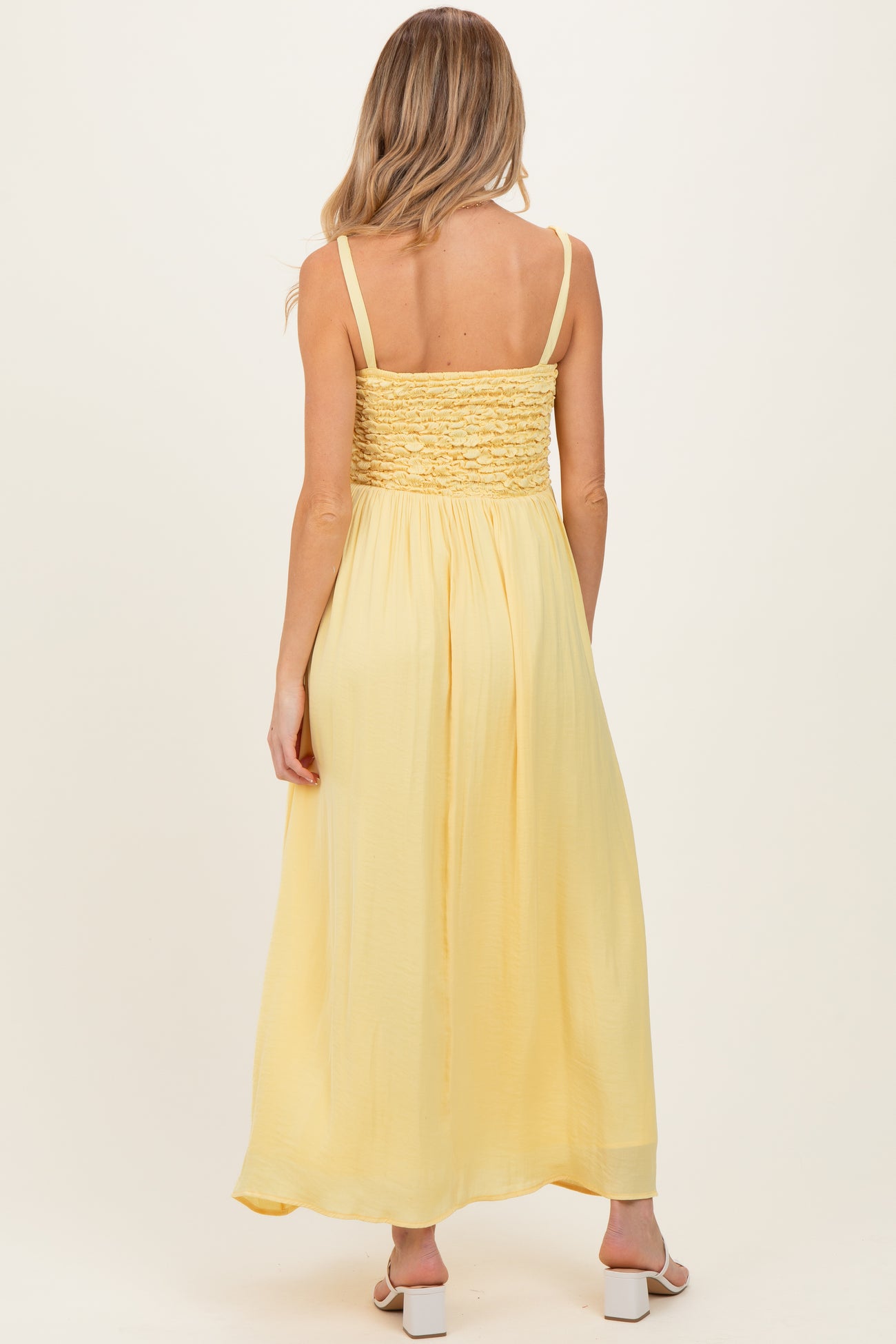 woman wearing a back view of a light yellow maternity maxi dress with smocked bodice and adjustable straps