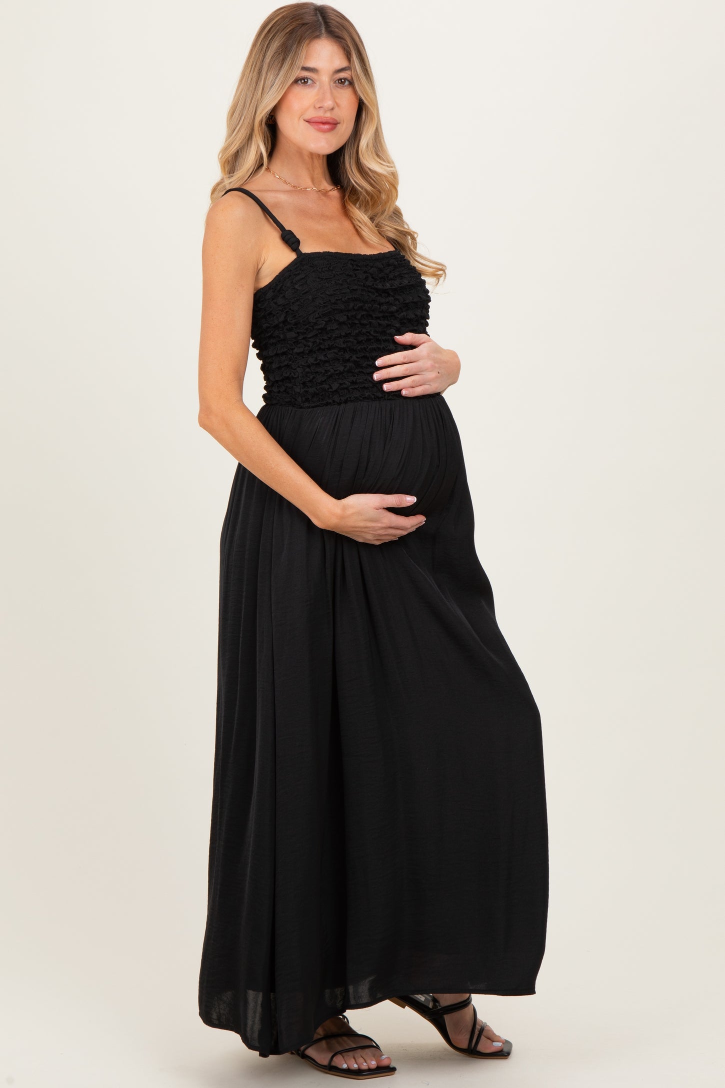 woman wearing a black maternity maxi dress with ruffled details and holding her baby bump
