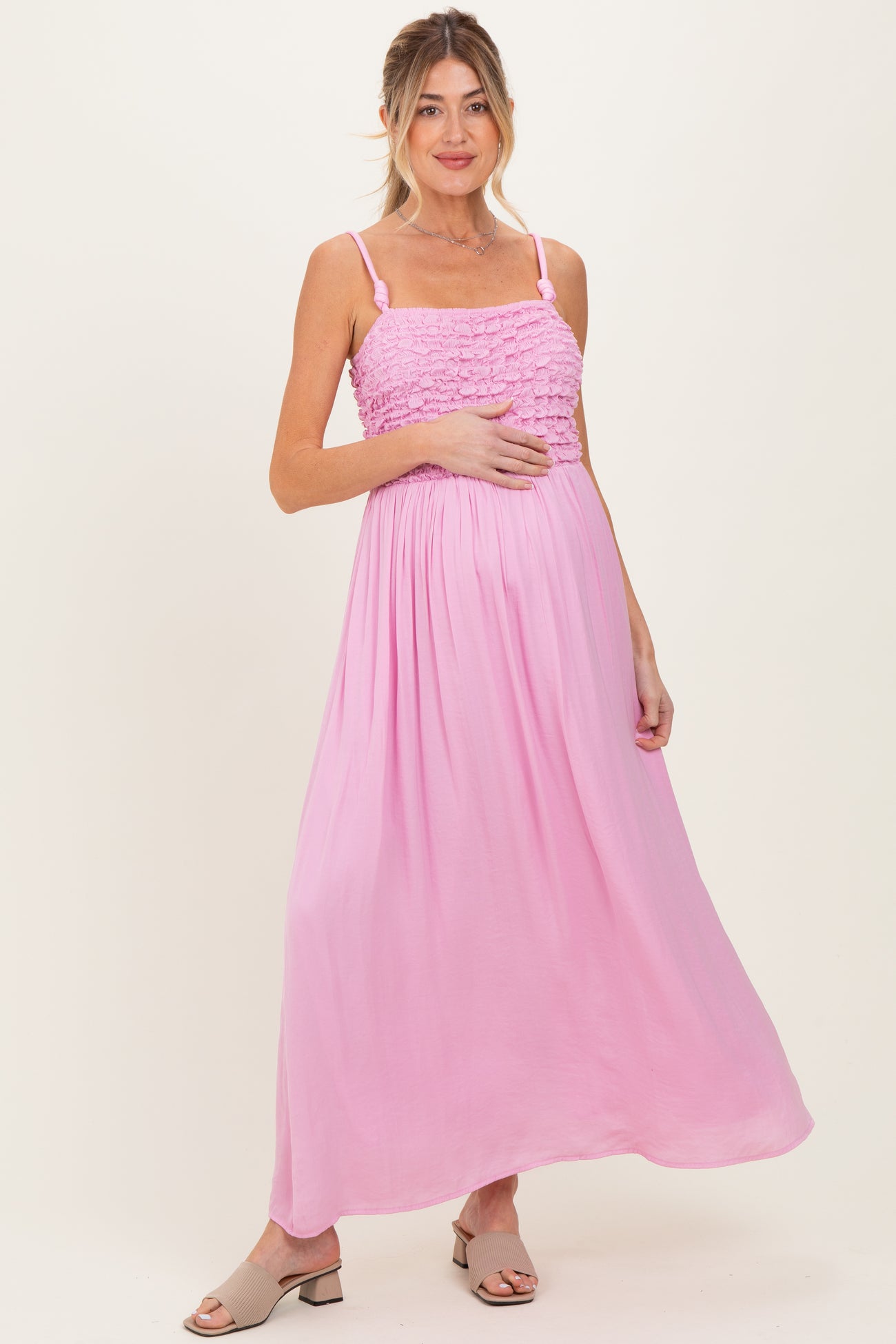 woman wearing a pink maternity maxi dress with smocked bodice and holding her baby bump