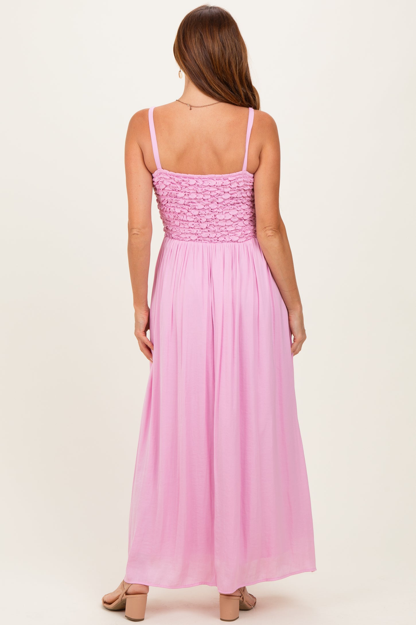 woman wearing a light pink backless maxi dress with a smocked bodice and adjustable straps