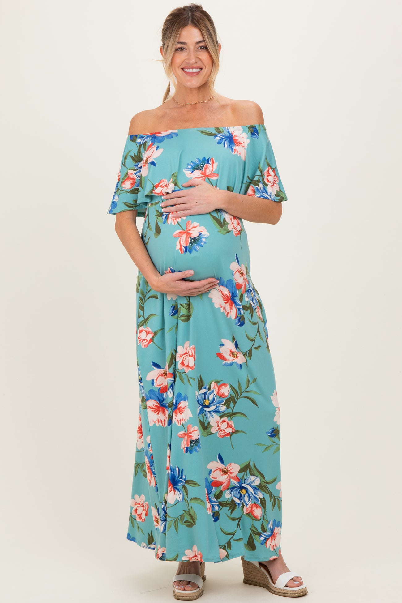 woman wearing a teal floral off-the-shoulder maternity dress and holding her baby bump