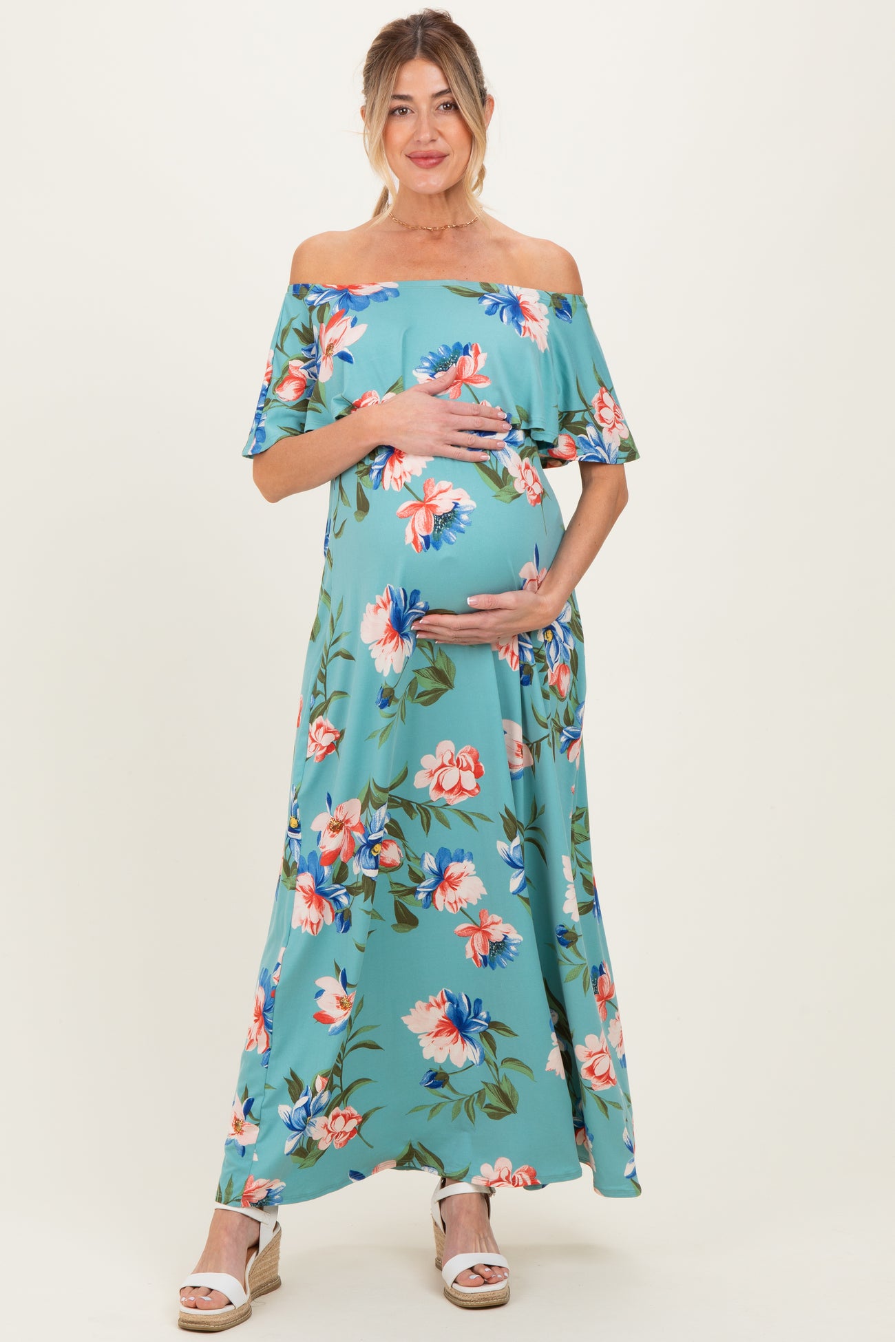 woman wearing a floral off-the-shoulder maternity maxi dress and cradling her baby bump