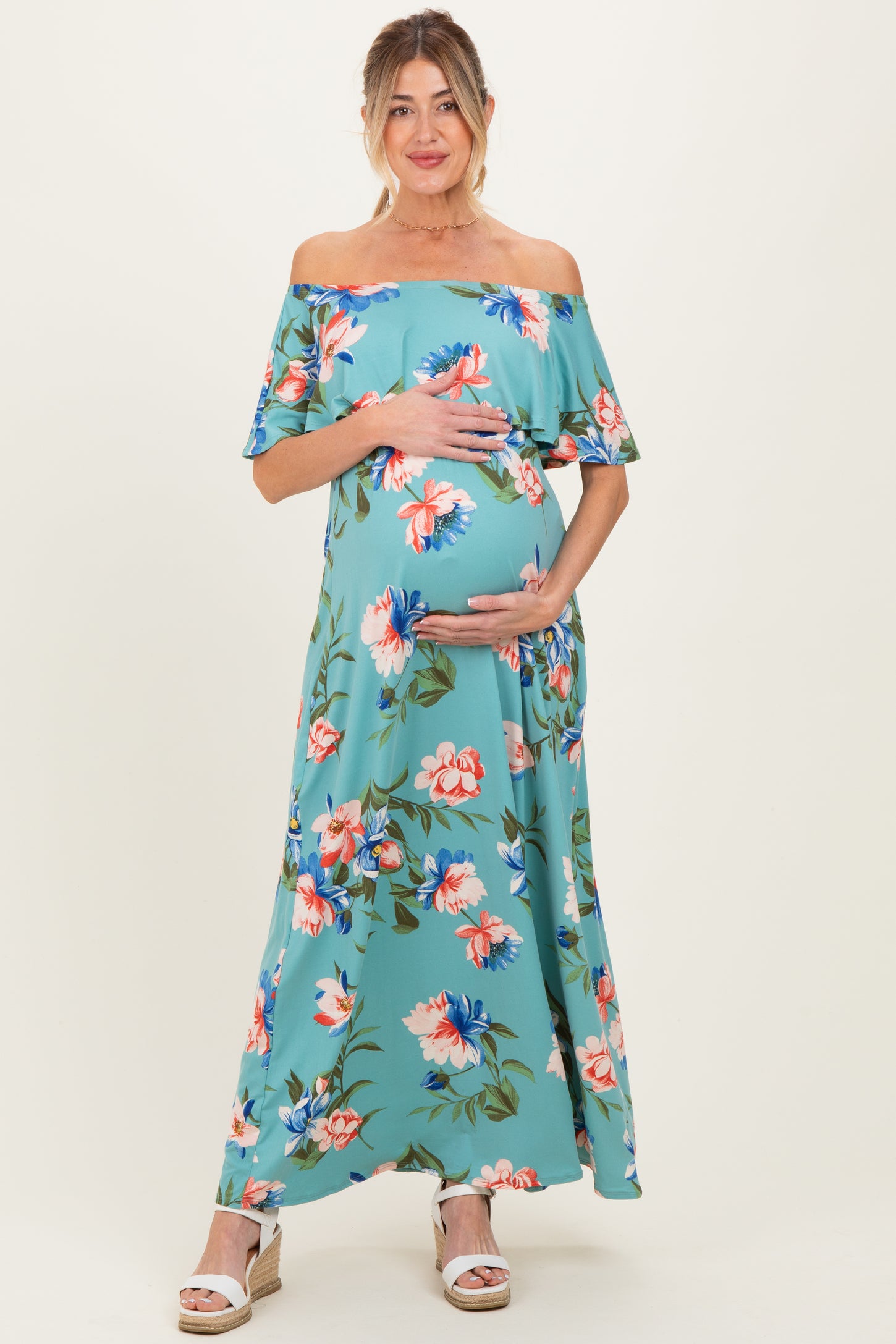 woman wearing a floral off-the-shoulder maternity maxi dress and cradling her baby bump