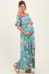 woman wearing a teal off-shoulder floral maternity maxi dress and holding her baby bump