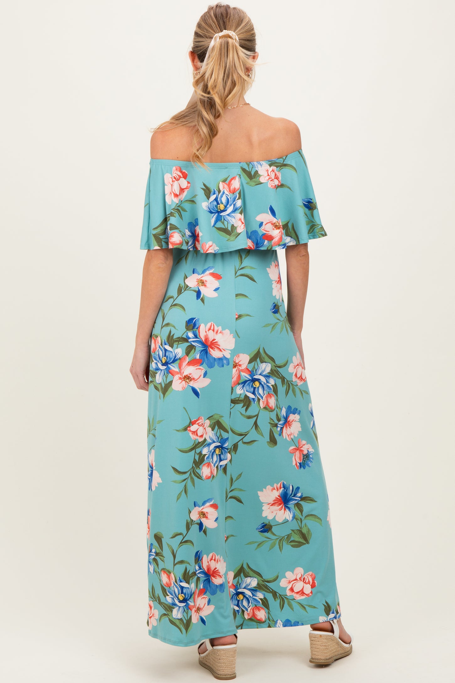 woman wearing a floral off-the-shoulder maternity maxi dress in turquoise with a flowy ruffle detail