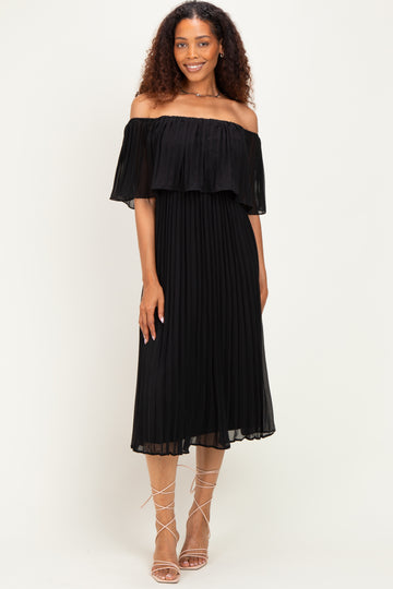 woman wearing a black off-the-shoulder pleated dress with a flowing ruffle detail and strappy sandals