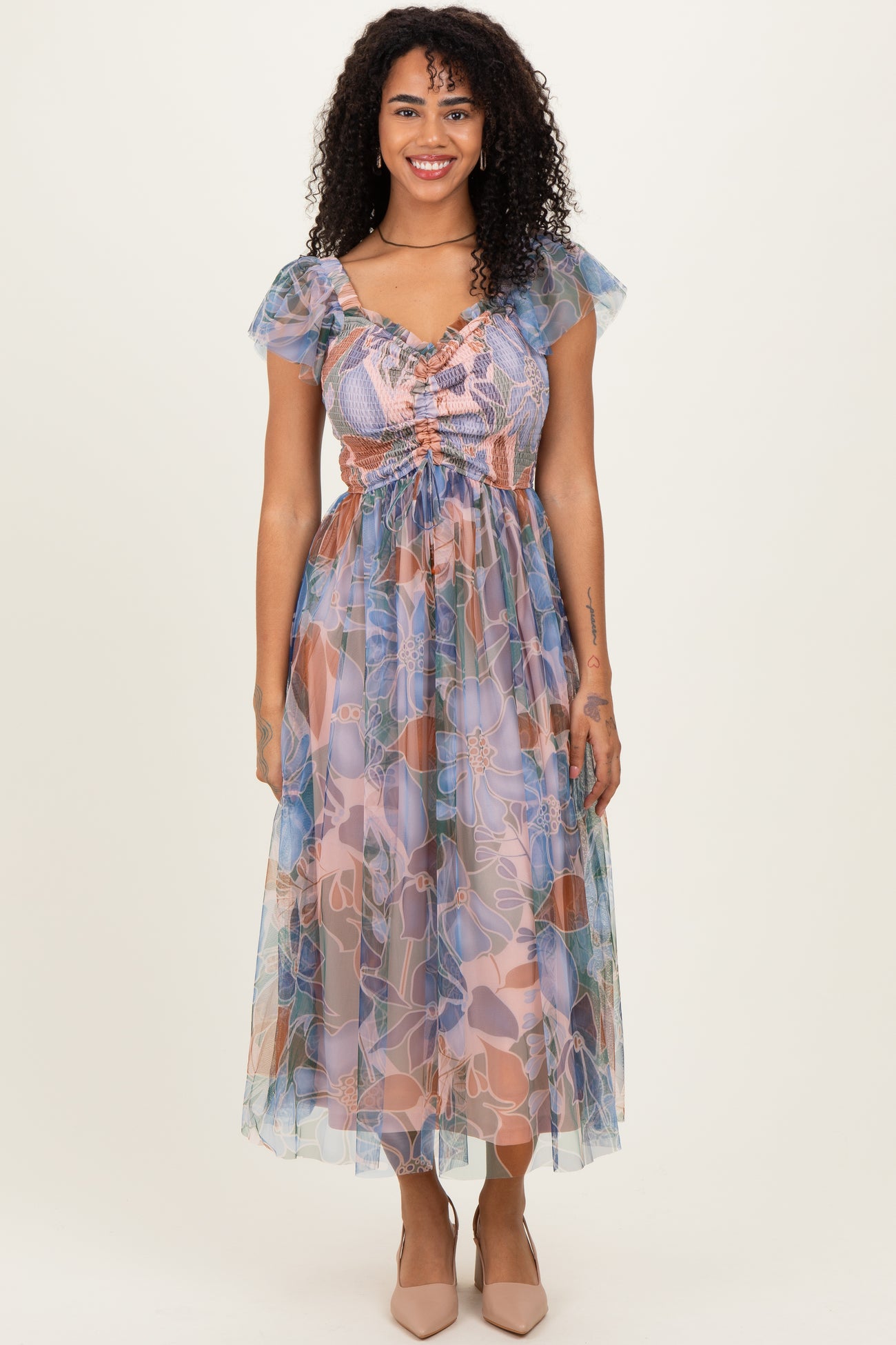 woman wearing a floral print maxi dress with ruffled sleeves and a cinched waist, standing against a neutral background