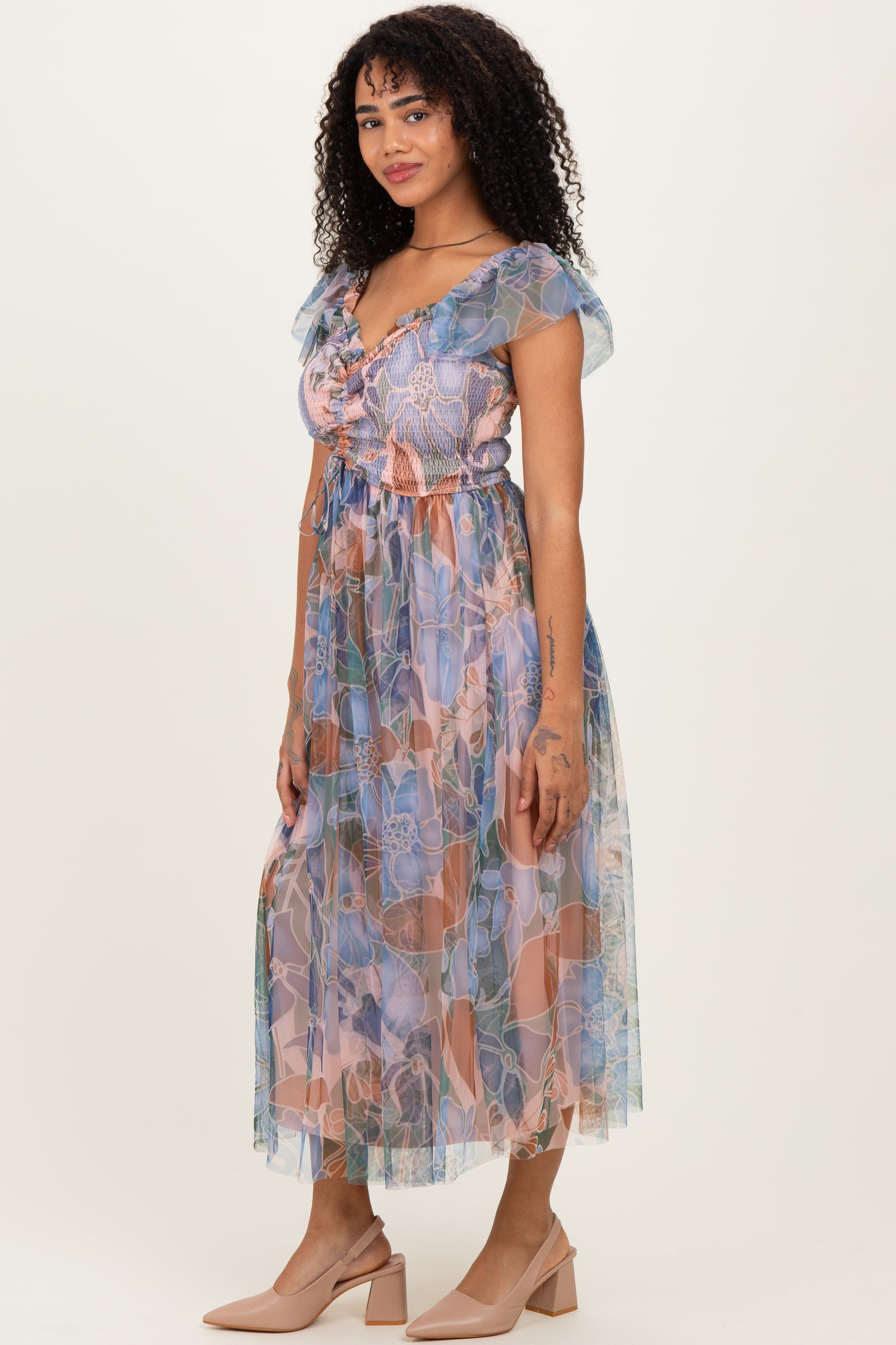 woman wearing a patterned pastel maxi dress with short ruffled sleeves and a cinched waist, styled with nude heels