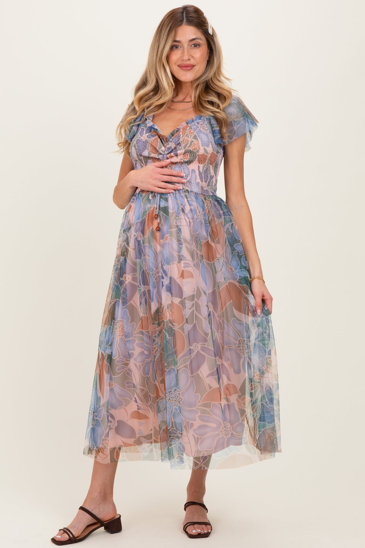 woman wearing a floral maternity dress with a sheer overlay and a baby bump visible