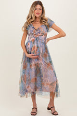woman wearing a floral print maternity dress with a flowy skirt and a baby bump visible, smiling and holding her belly