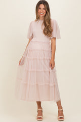 woman wearing a light pink maternity dress with sheer flutter sleeves and tiered lace accents