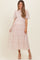 woman wearing a light pink maternity dress with sheer flutter sleeves and tiered lace accents