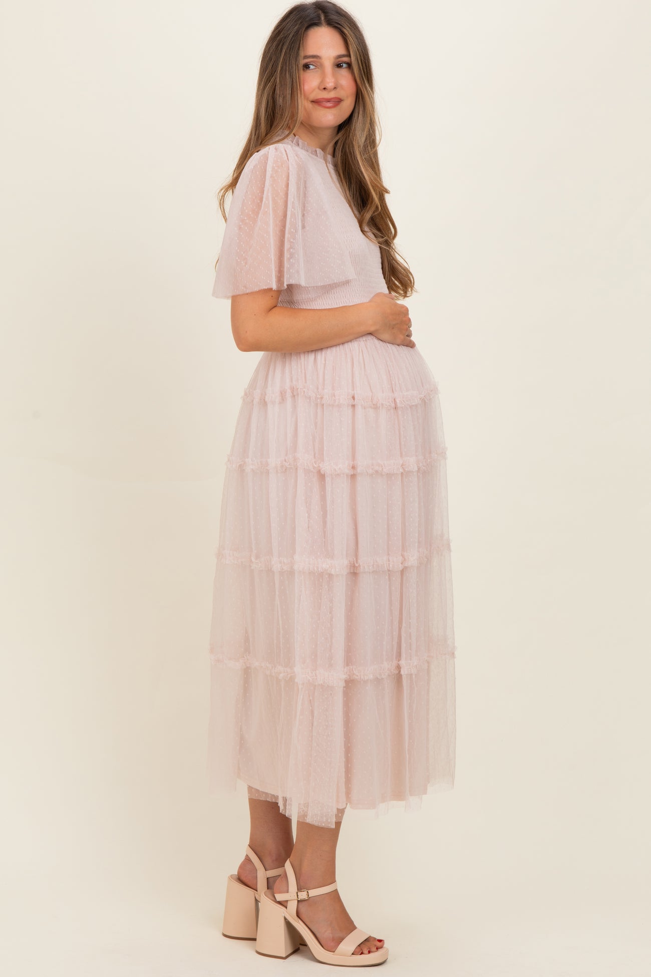 woman wearing a light pink maternity maxi dress with tiered ruffles, holding her baby bump
