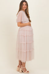 woman wearing a light pink maternity maxi dress with tiered ruffles, holding her baby bump