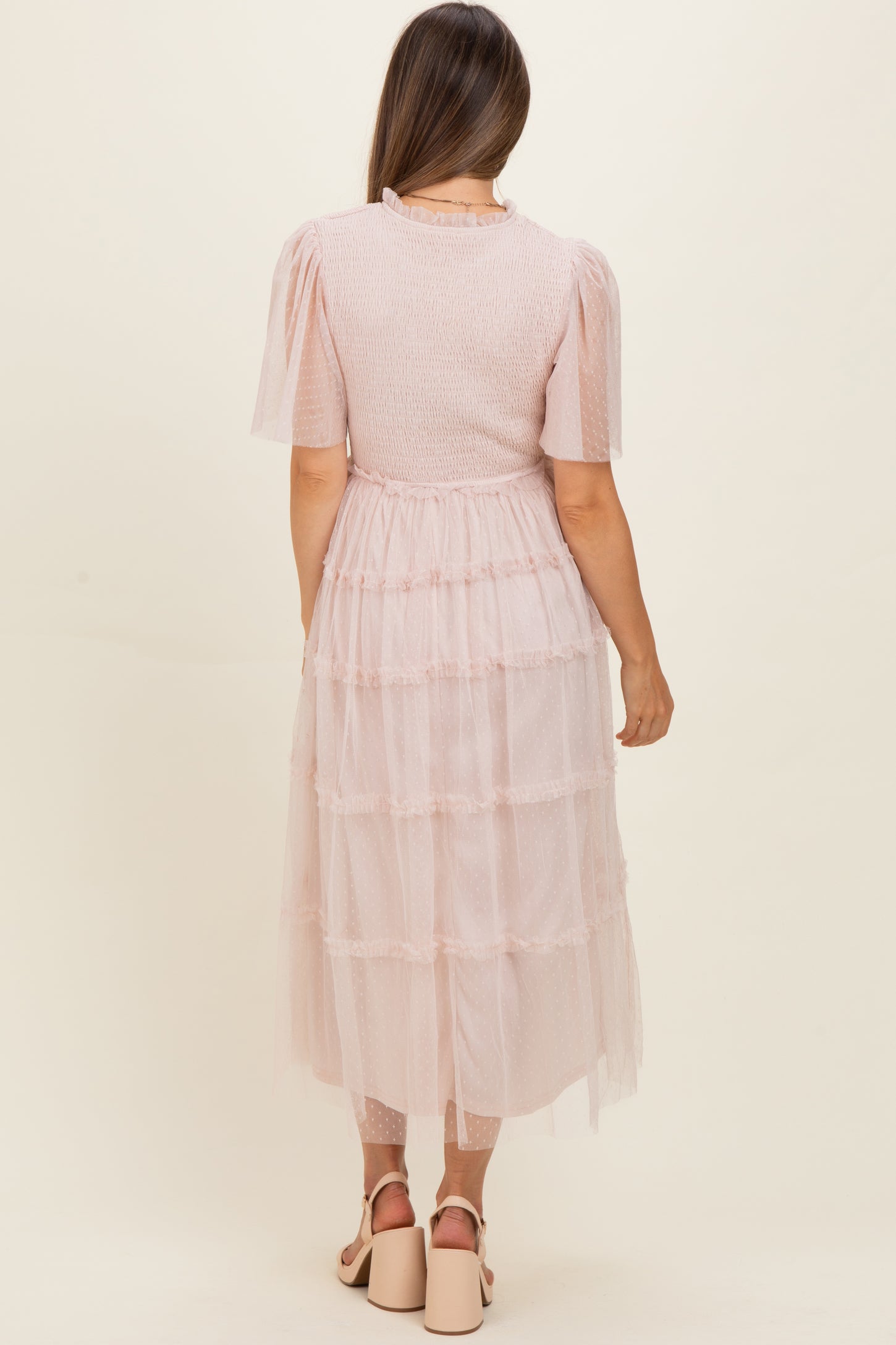 woman wearing a pink tiered maternity dress with short puff sleeves and a ruffled hem, showing her baby bump from the back