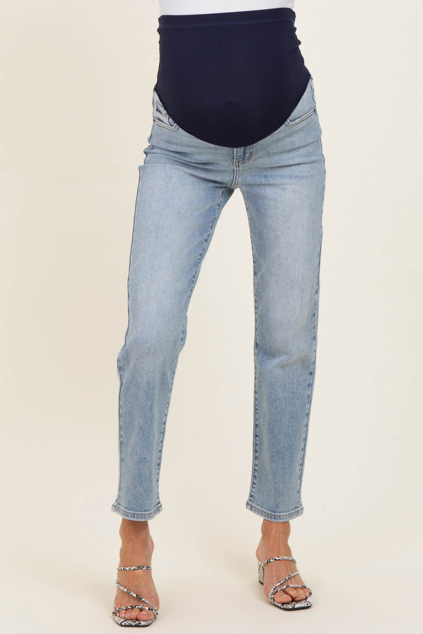 woman wearing light wash maternity jeans with a navy blue over-the-bump waistband and heels