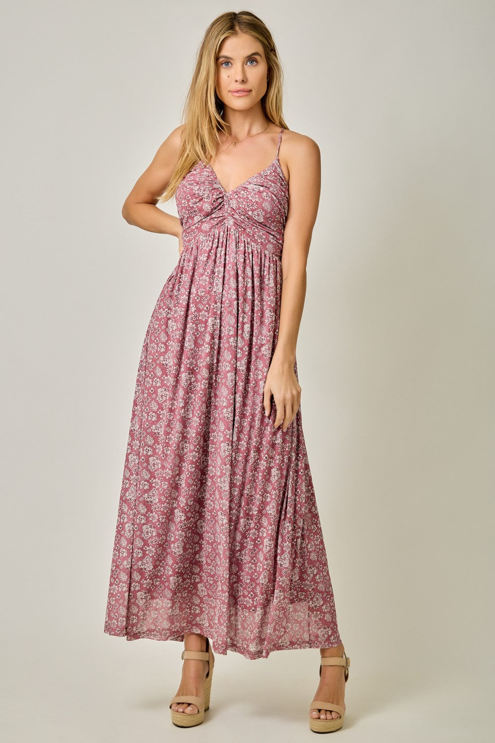 woman wearing a floral patterned maxi dress in shades of pink with a twisted front detail and spaghetti straps