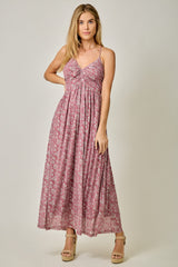 woman wearing a floral patterned maxi dress in shades of pink with a twisted front detail and spaghetti straps