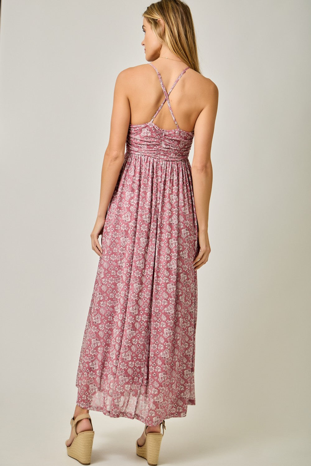 woman wearing a pink floral maxi dress with crisscross straps and a flowy skirt, viewed from the back