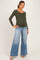 woman wearing an olive green long sleeve maternity top and light wash wide-leg jeans, showing her baby bump