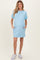 woman wearing a light blue short sleeve maternity dress with a pocket and side pockets, showing her baby bump