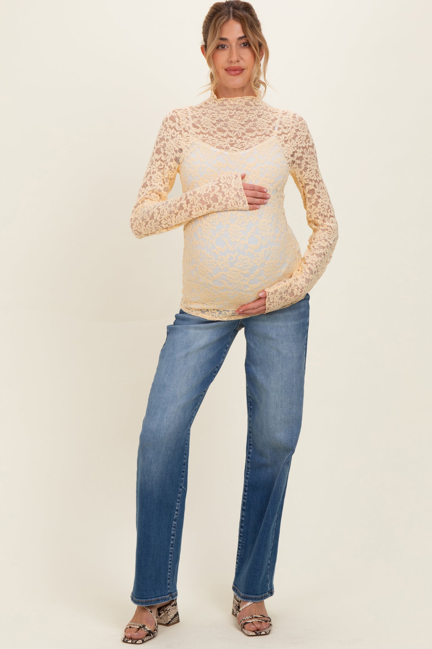 woman wearing a yellow lace long sleeve maternity top while holding her baby bump, paired with light blue jeans