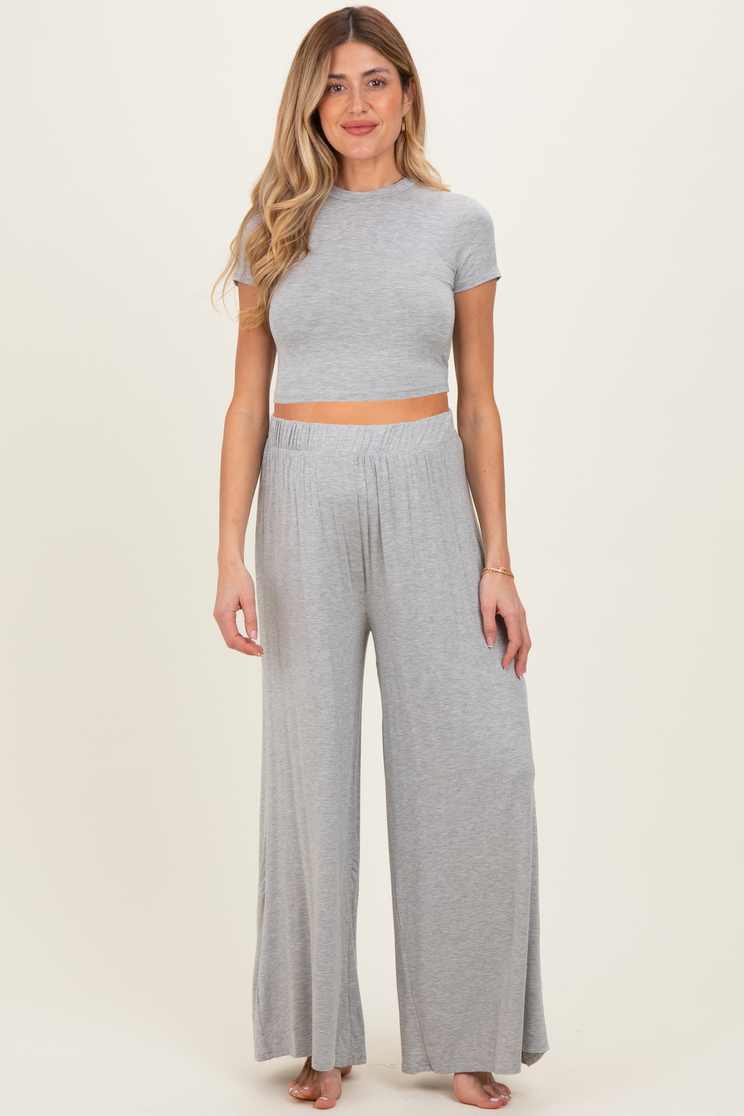woman wearing a light gray maternity crop top and wide-leg pants, showcasing her baby bump