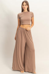 woman wearing a brown cropped top and wide-leg pants, standing against a neutral background