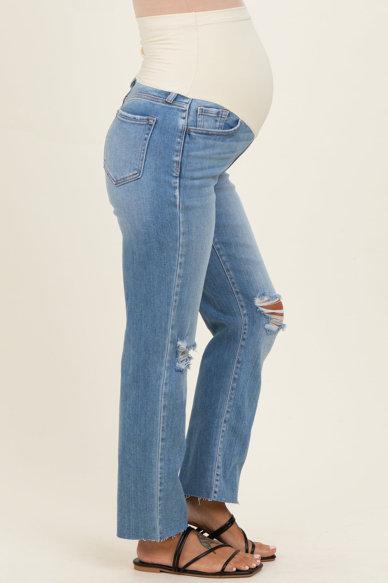 woman wearing light blue distressed maternity jeans with a fitted waistband, showing a visible baby bump
