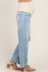 woman wearing light blue distressed maternity jeans and a beige top, showcasing her baby bump