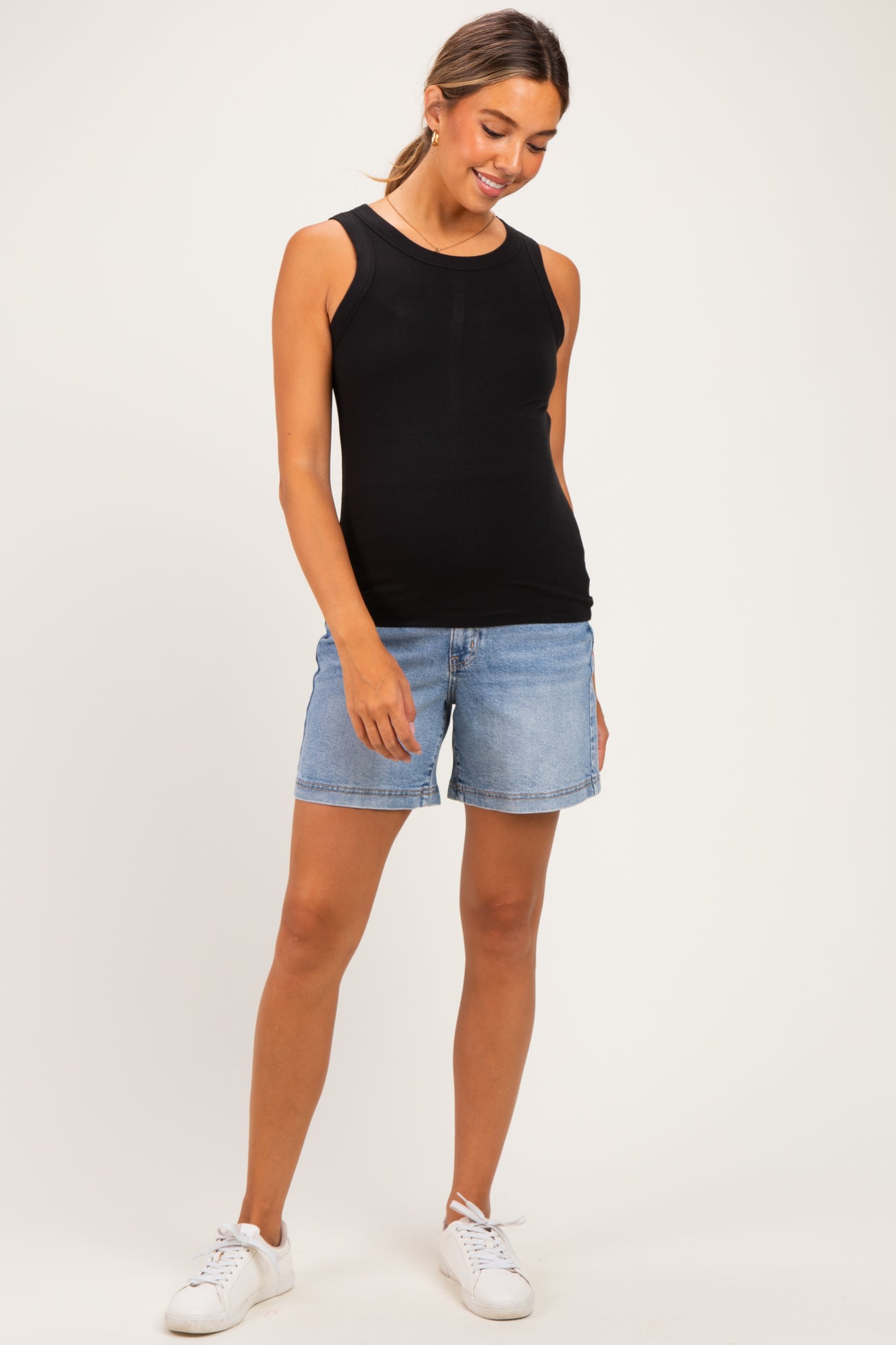 woman wearing a black maternity tank top and denim shorts, with a visible baby bump