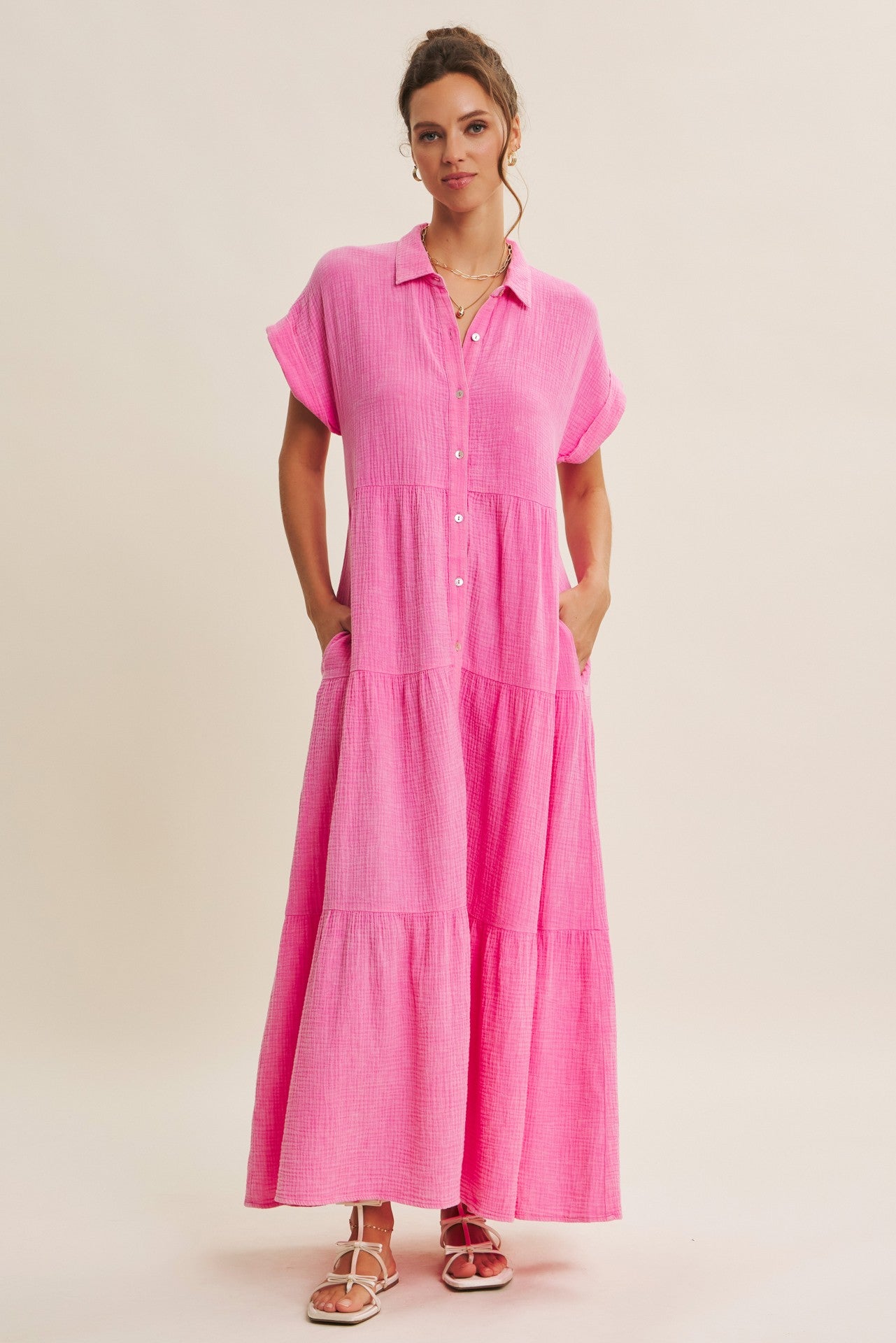 woman wearing a pink button-up maxi dress with short sleeves and pockets, standing against a neutral background