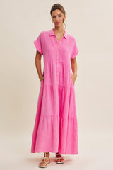 woman wearing a pink button-up maxi dress with short sleeves and pockets, standing against a neutral background