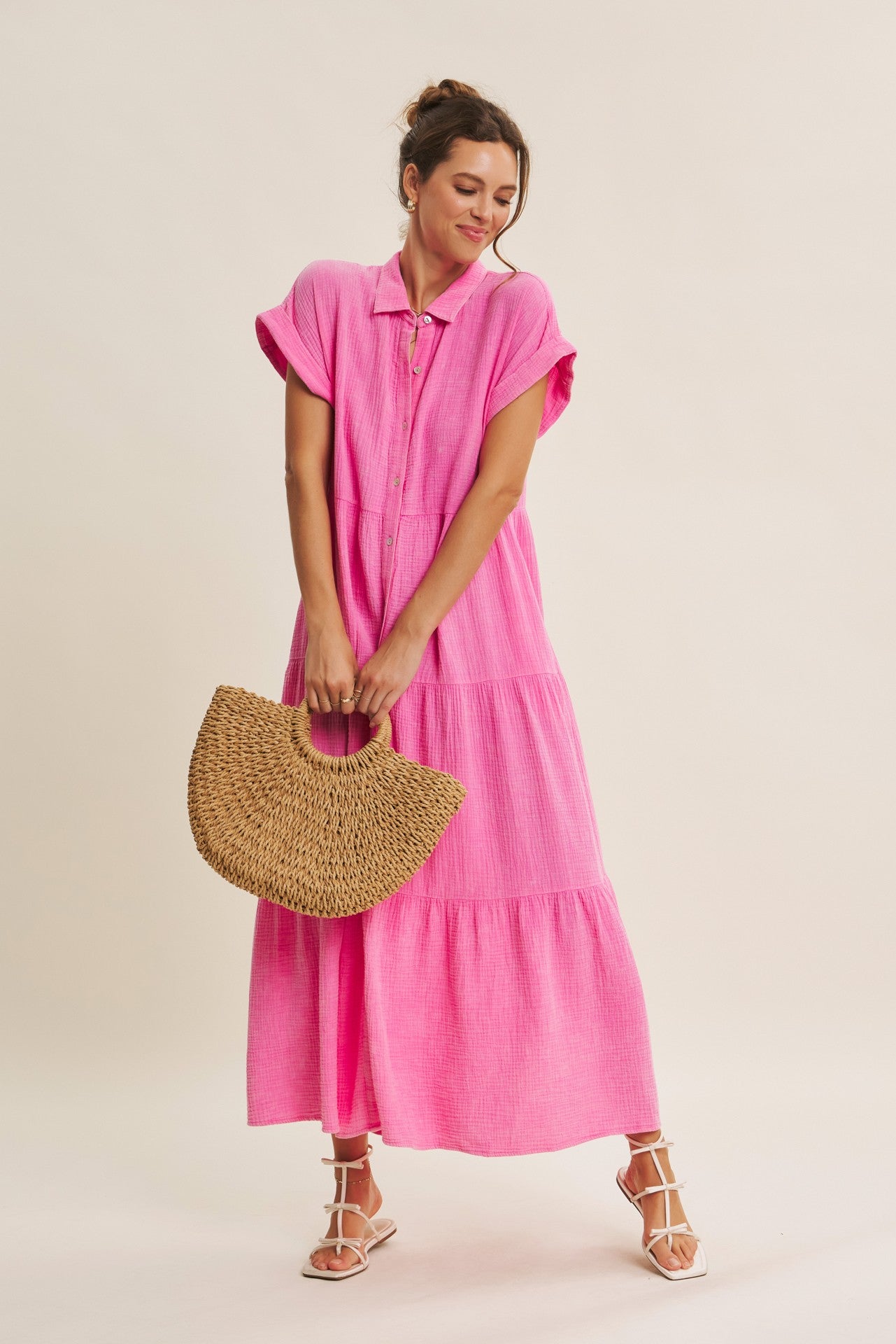 woman wearing a bright pink tiered maxi dress with short sleeves and a collar, holding a woven handbag