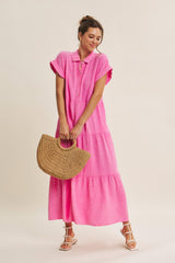 woman wearing a bright pink tiered maxi dress with short sleeves and a collar, holding a woven handbag