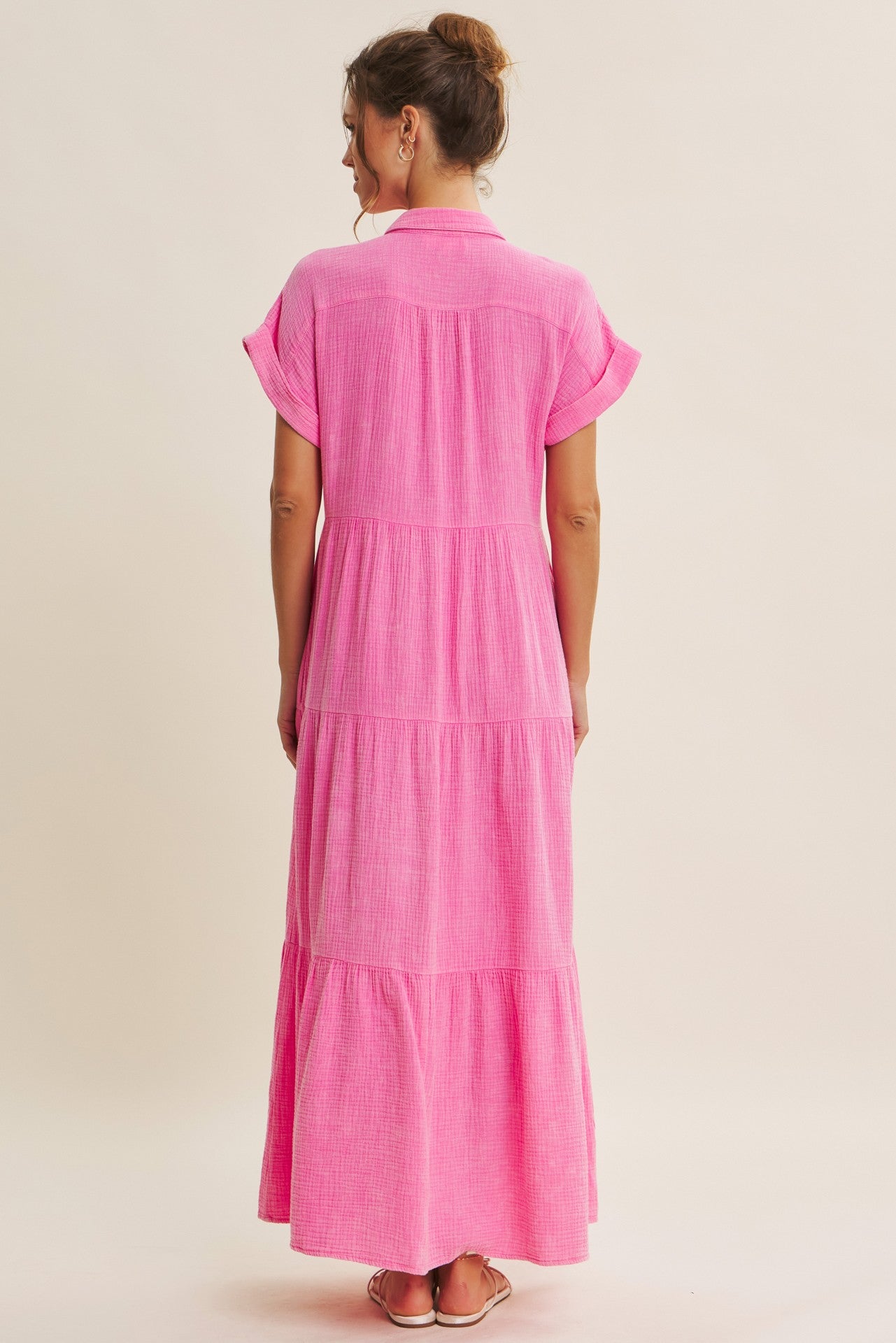 woman wearing a bright pink maxi dress with short sleeves and a tiered design, viewed from the back