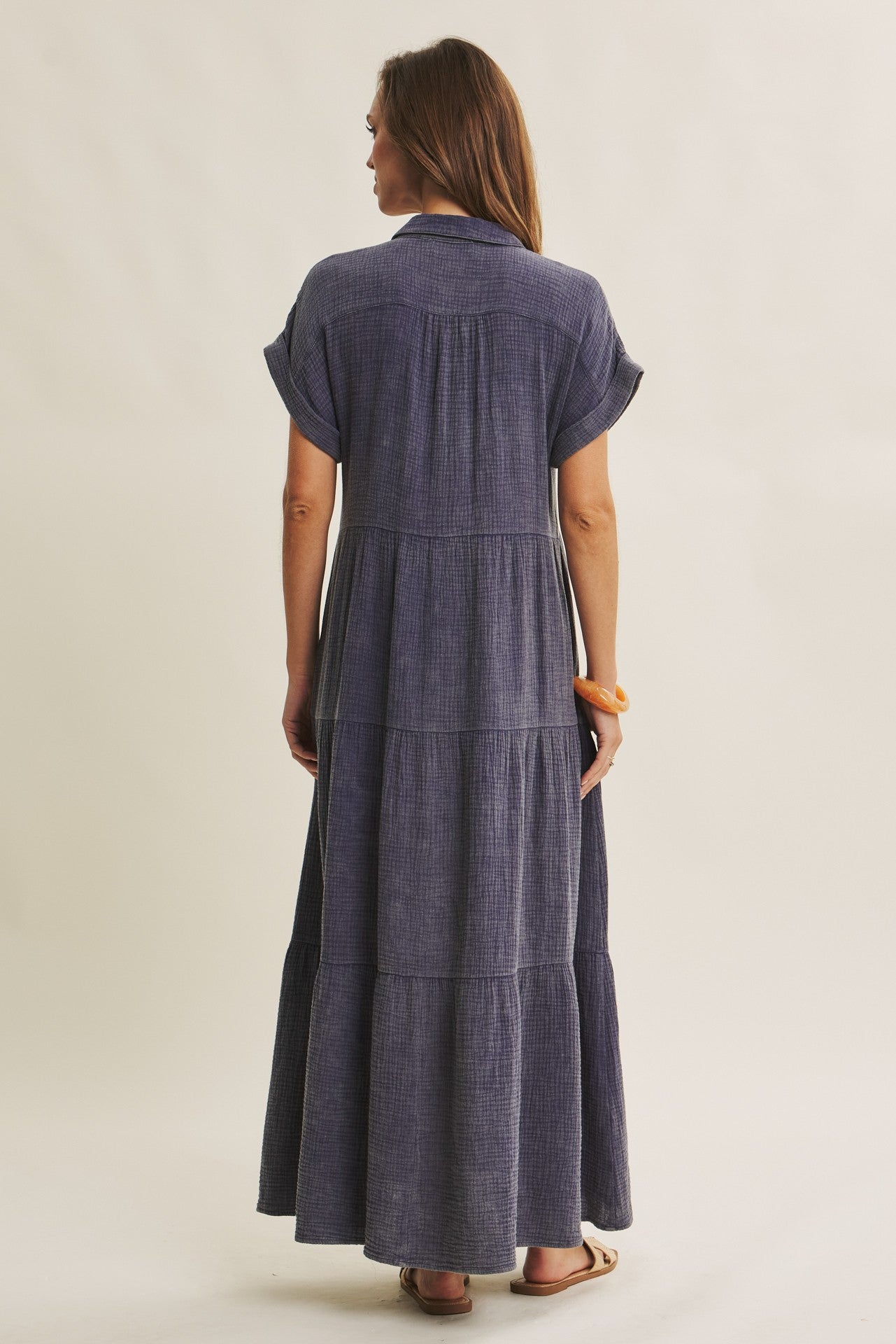 woman wearing a navy blue tiered maxi dress with short sleeves and a collared neckline, shown from the back