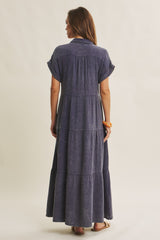 woman wearing a navy blue tiered maxi dress with short sleeves and a collared neckline, shown from the back