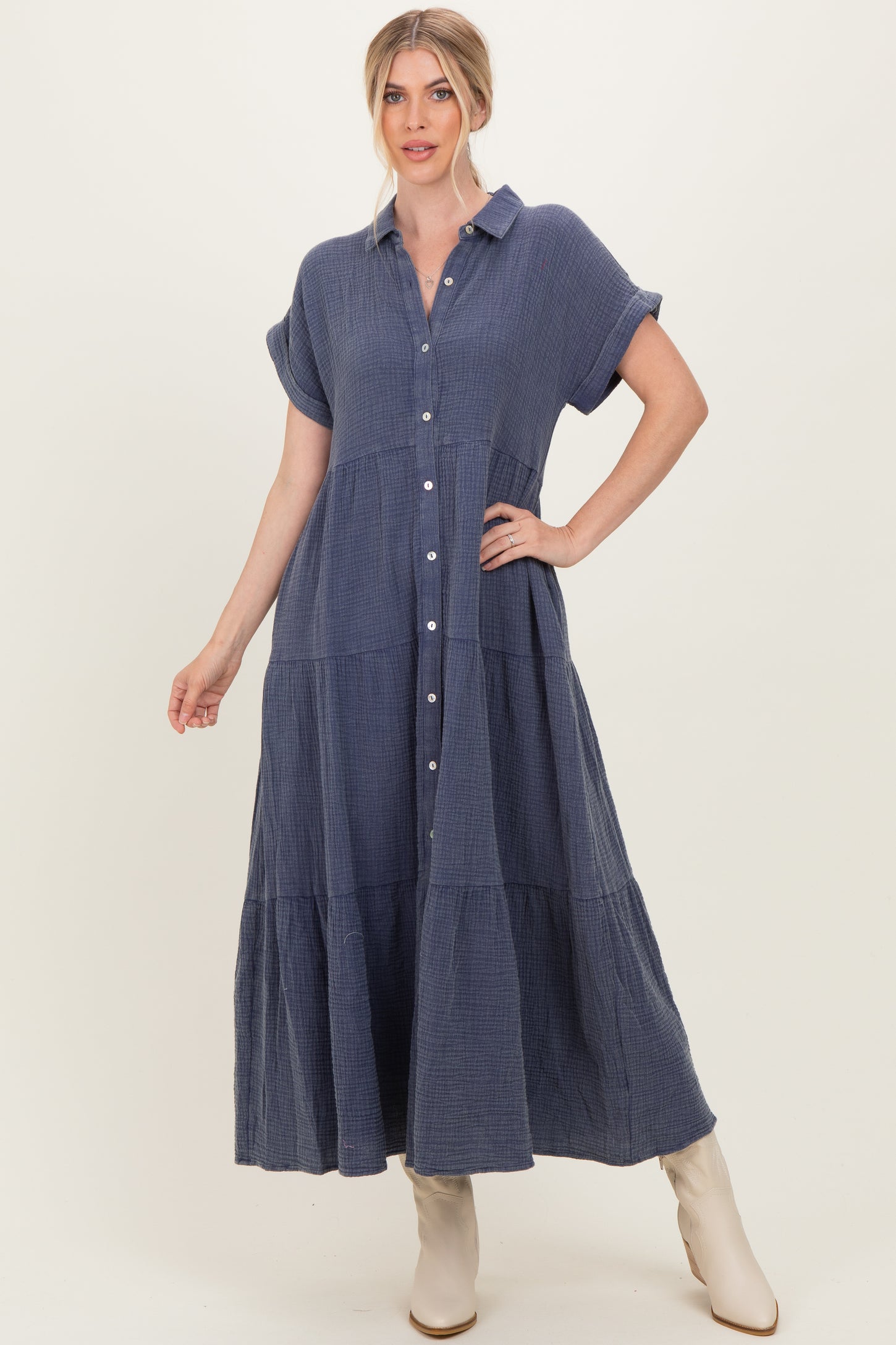 woman wearing a navy blue button-down maxi dress with short sleeves and tiered details, standing against a neutral background