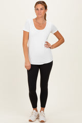 woman wearing a white short sleeve scoop neck top and black leggings, standing with hands on hips