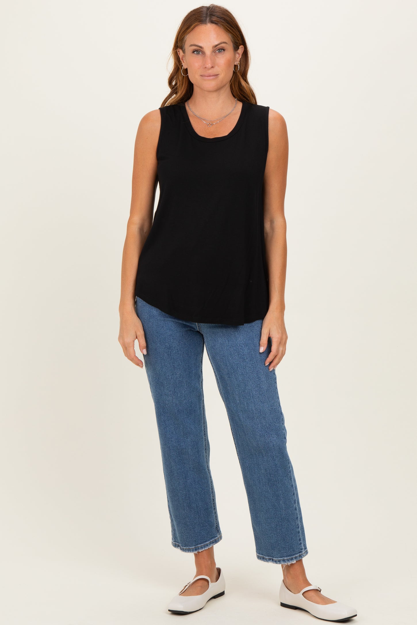 woman wearing a black sleeveless top with a rounded hem and blue high-waisted straight leg jeans