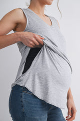 woman wearing a gray sleeveless maternity top, pulling it to reveal a black inner layer and a visible baby bump