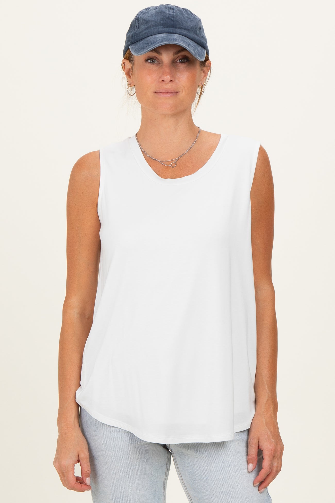 woman wearing a white sleeveless top with a v-neck and light blue jeans, paired with a navy baseball cap