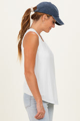 woman wearing a white sleeveless top and a navy blue cap, side view with long hair in a ponytail