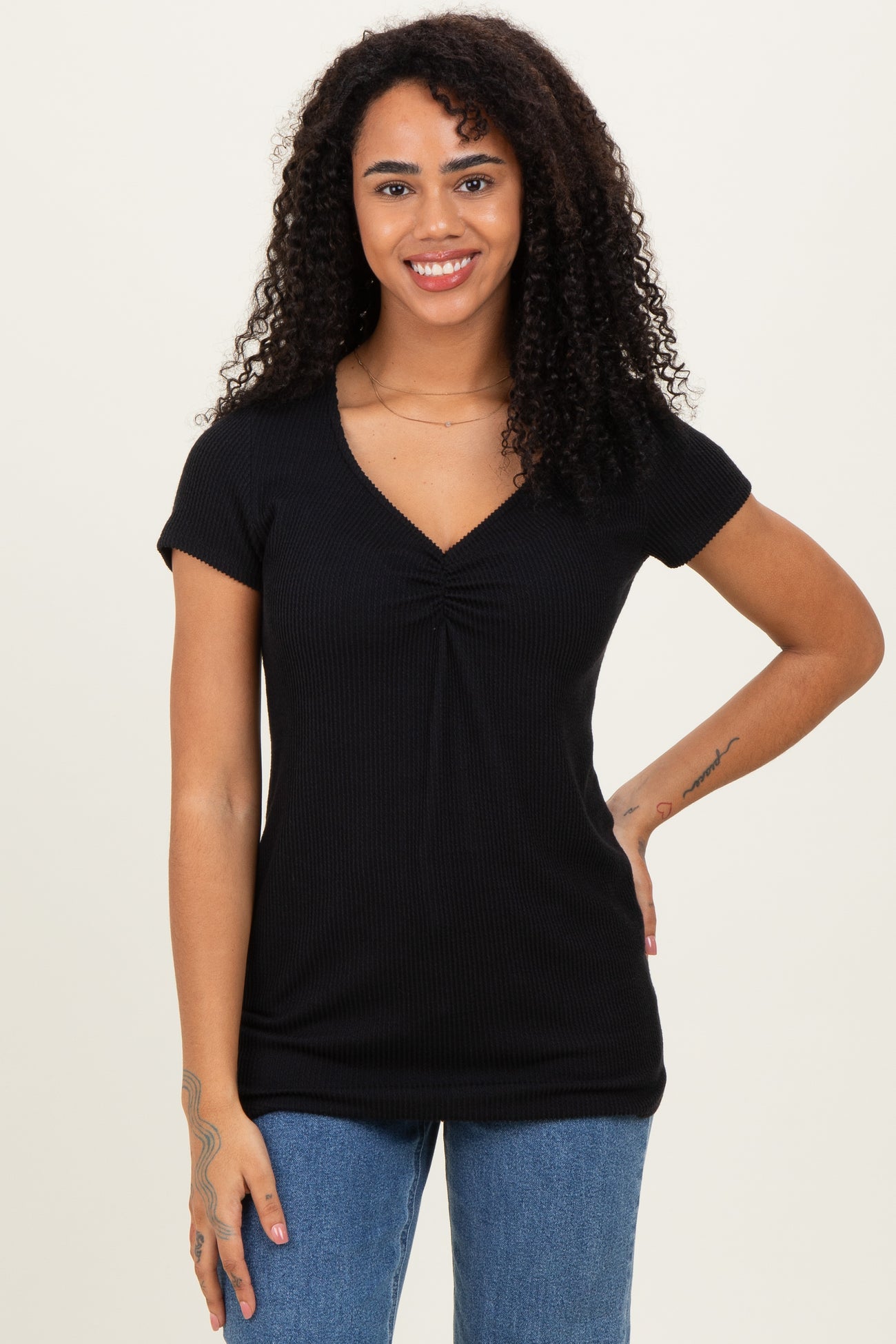 woman wearing a black short sleeve top with a ruched v-neck and standing with one hand on her hip