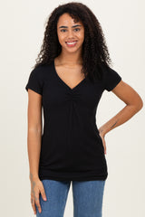 woman wearing a black short sleeve top with a ruched v-neck and standing with one hand on her hip
