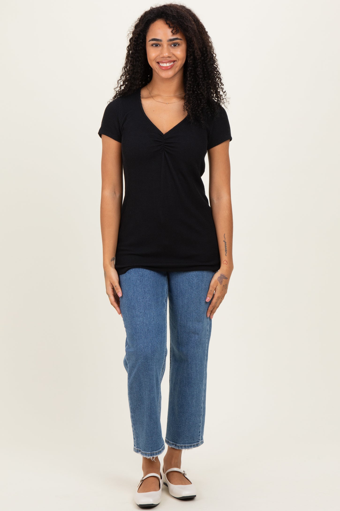 woman wearing a black short sleeve top with a v-neck and gathered detail, paired with blue straight-leg jeans