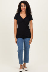 woman wearing a black short sleeve top with a v-neck and gathered detail, paired with blue straight-leg jeans